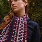 Person wearing a dark sweater and berry coloured patterned scarf standing in a forest setting