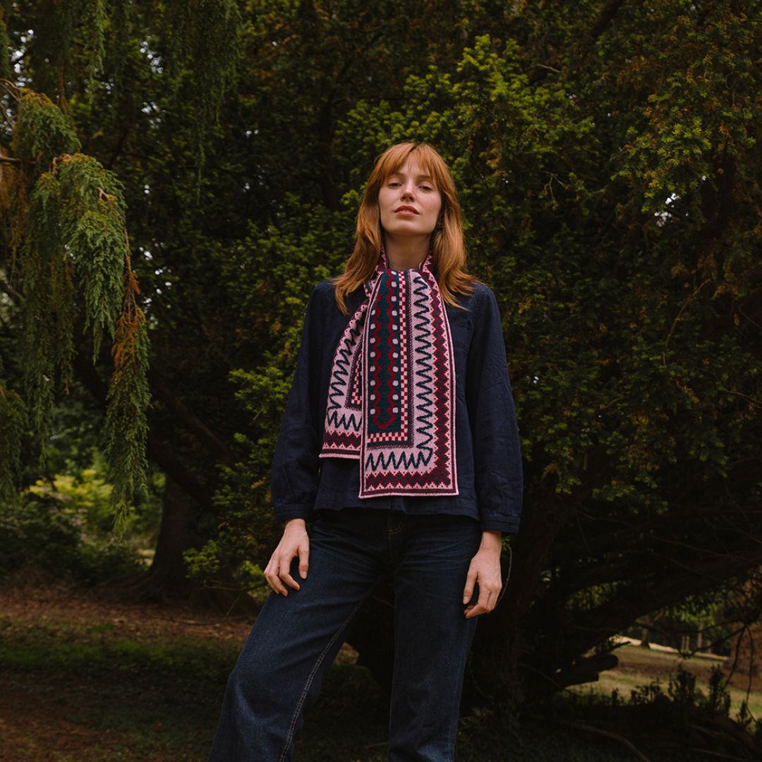 Person wearing a dark sweater and berry coloured patterned scarf standing in a forest setting