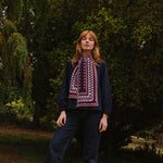Person wearing a dark sweater and berry coloured patterned scarf standing in a forest setting