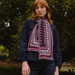 Person wearing a dark sweater and berry coloured patterned scarf standing in a forest setting
