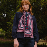 Person wearing a dark sweater and berry coloured patterned scarf standing in a forest setting