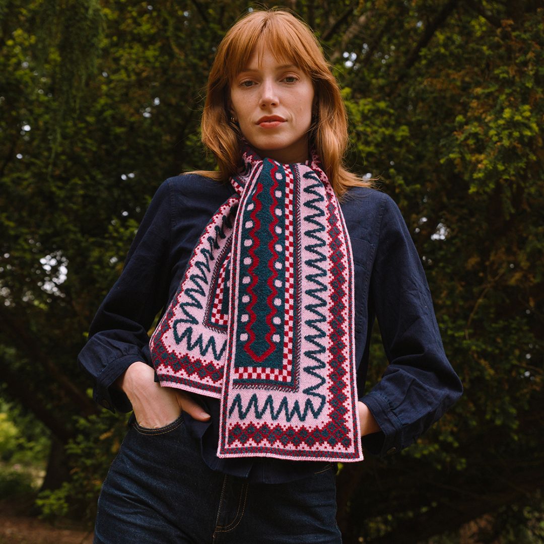 Person wearing a dark sweater and berry coloured patterned scarf standing in a forest setting
