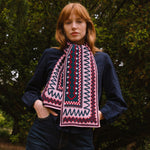 Person wearing a dark sweater and berry coloured patterned scarf standing in a forest setting