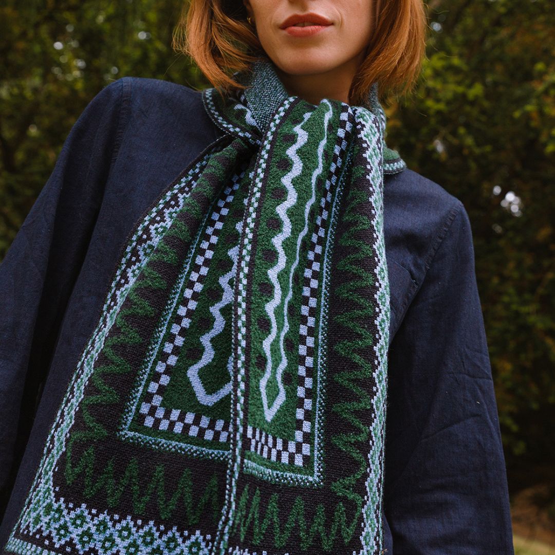 Person wearing a dark blue jacket with a green patterned scarf against a blurred natural background
