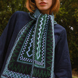Person wearing a dark blue jacket with a green patterned scarf against a blurred natural background