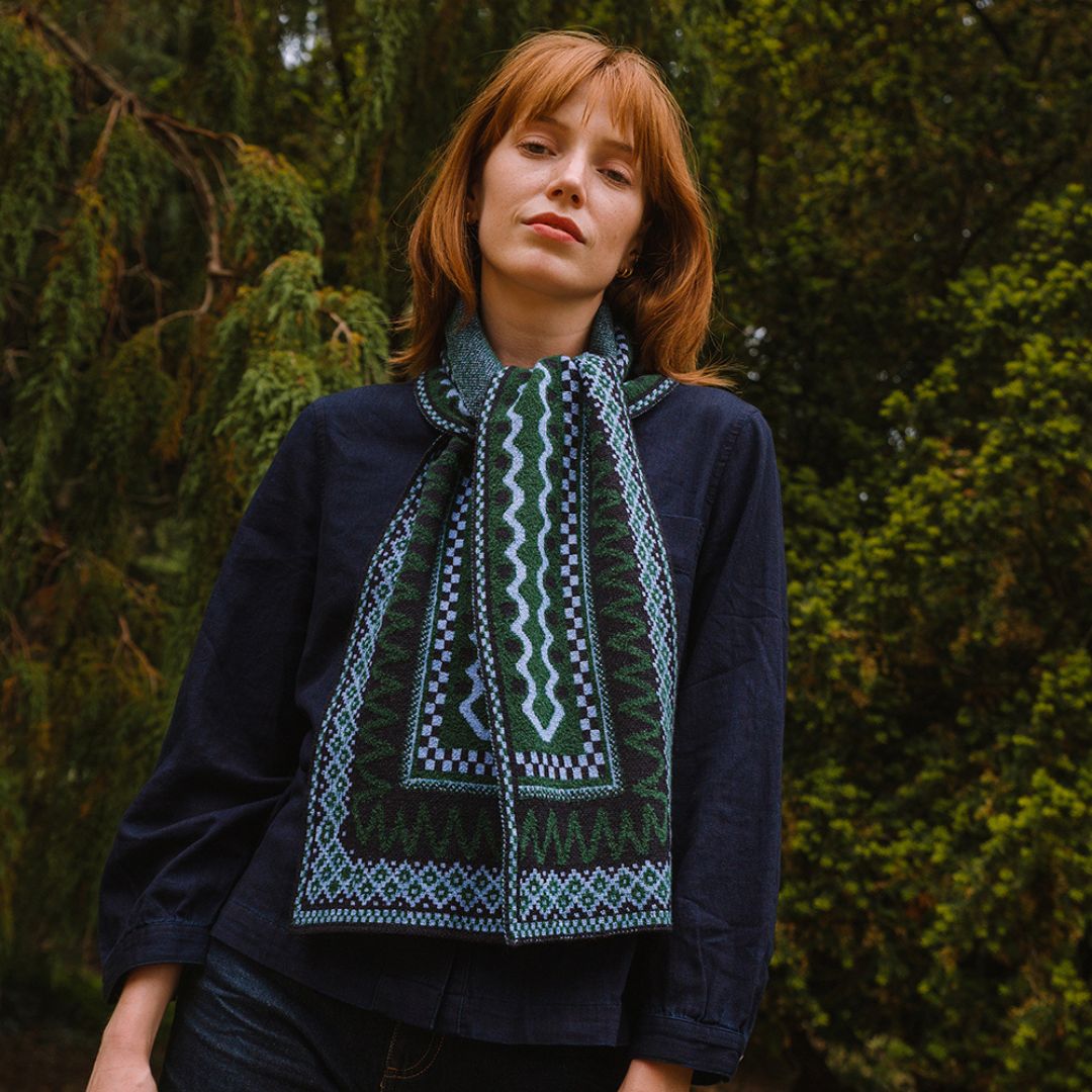 woman standing in the woods wearing a blue and green patterned scarf.