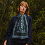 woman standing in the woods wearing a blue and green patterned scarf.