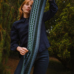 Person holding a long, patterned scarf outdoors with greenery in the background
