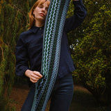 Person holding a long, patterned scarf outdoors with greenery in the background