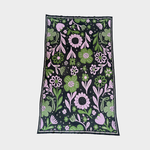 A knitted blanket with a dense floral pattern on a black background, featuring pink and green flowers, leaves, and stems, bordered by a thin dark edge, shown flat against a light gray background.