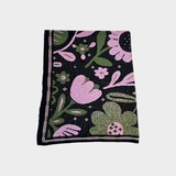 A square dark blue blanket featuring a vibrant floral pattern in pink and green, with a decorative striped border, displayed flat against a light gray background.
