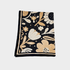 A folded square blanket in a floral pattern in beige, cream, and black, displayed flat against a light gray background.