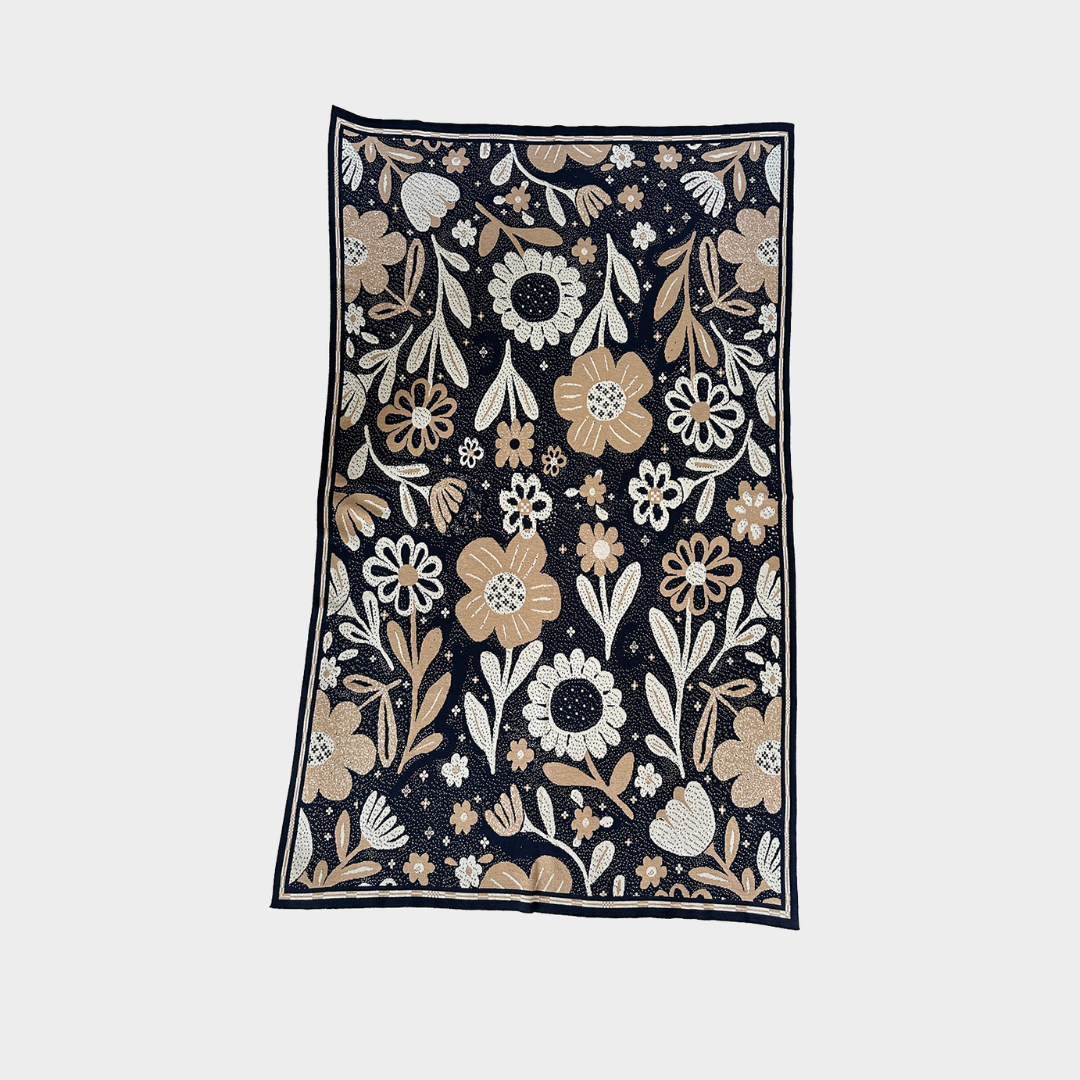 A rectangular blanket featuring a dense floral and botanical pattern on a dark navy background, with cream, beige, and light brown flowers and leaves, shown flat against a light gray background.