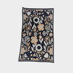 A rectangular blanket featuring a dense floral and botanical pattern on a dark navy background, with cream, beige, and light brown flowers and leaves, shown flat against a light gray background.