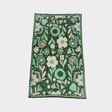A blanket with an all-over floral pattern, shown flat against a light gray background. The design features a dark forest green base with large and small flowers, leaves, and stems in mint green, cream, and white.