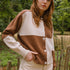 Woman wearing a brown and beige cardigan outdoors with greenery in the background