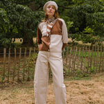 Person wearing a brown and white cardigan with a scarf, standing in a field with trees in the background.