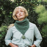 a woman standing beside a bush wearing a green cable knit scarf.