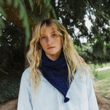 A lady standing in a forest wearing a blue cable knit scarf.