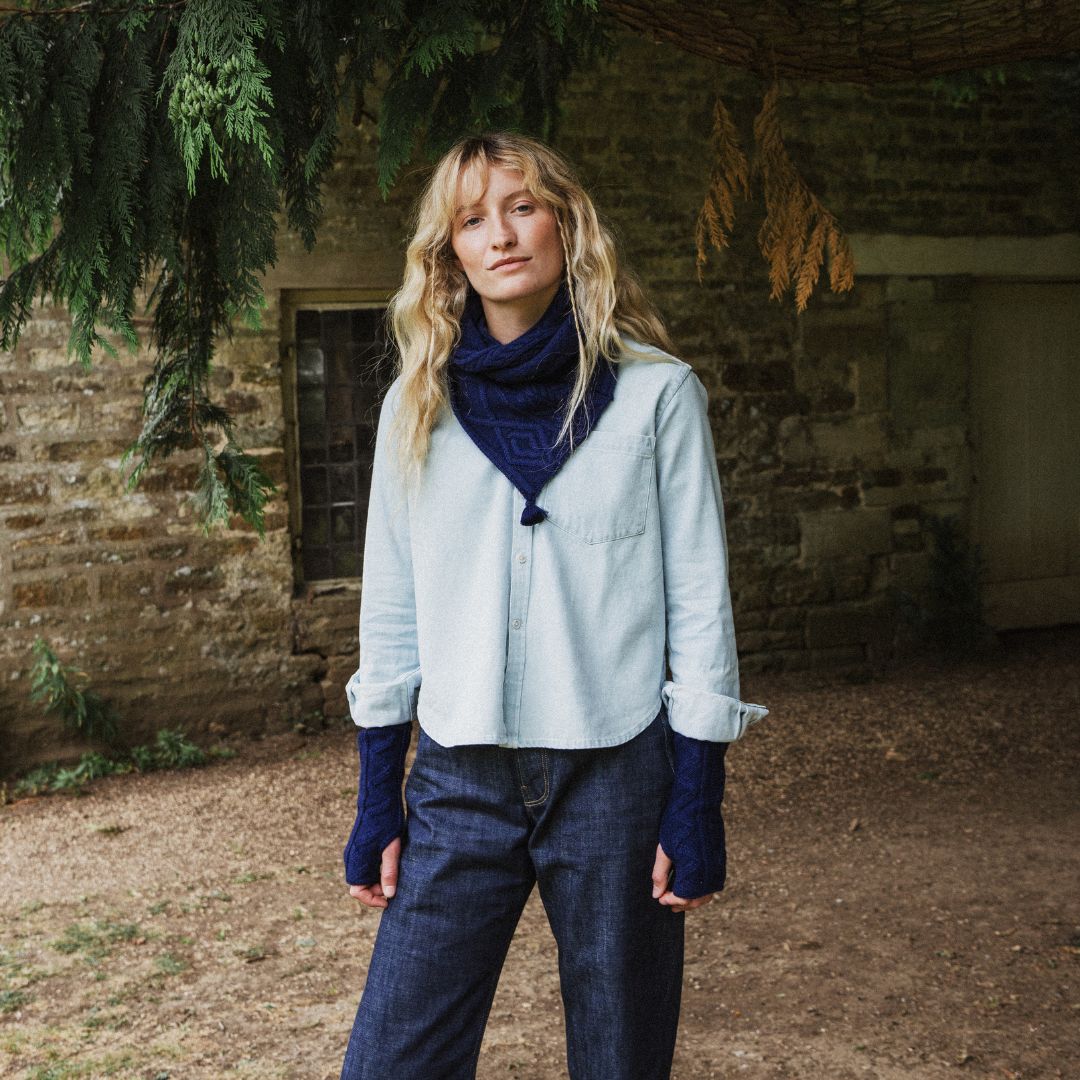 Woman standing in a park wearing a blue cable knit scarf and wrist warmers