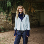 Woman standing in a park wearing a blue cable knit scarf and wrist warmers