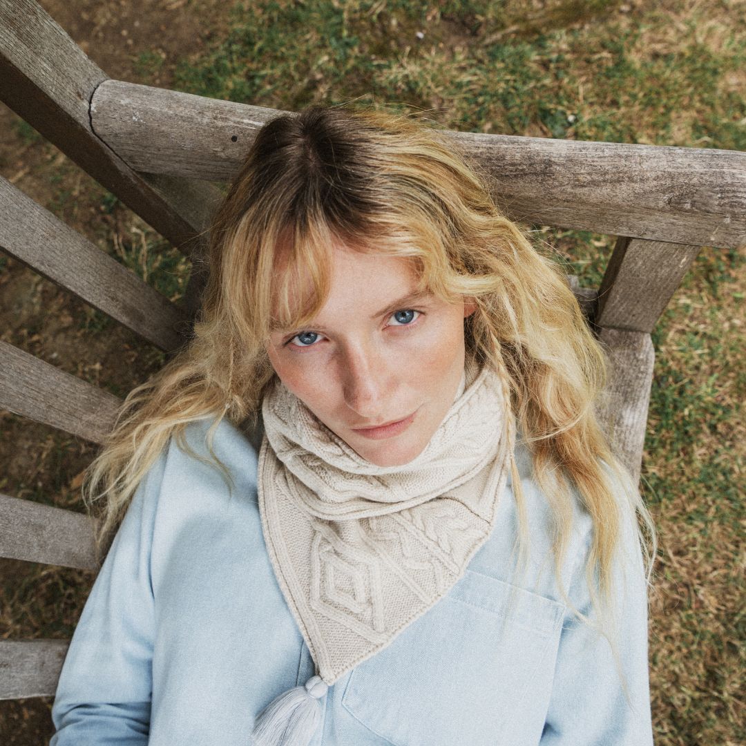 a close up iof a woman looking up, wearing a ream cable knit scarf.