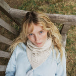 a close up iof a woman looking up, wearing a ream cable knit scarf.