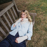 a woman lying on a bench wearing a cream scarf and blue jeans.