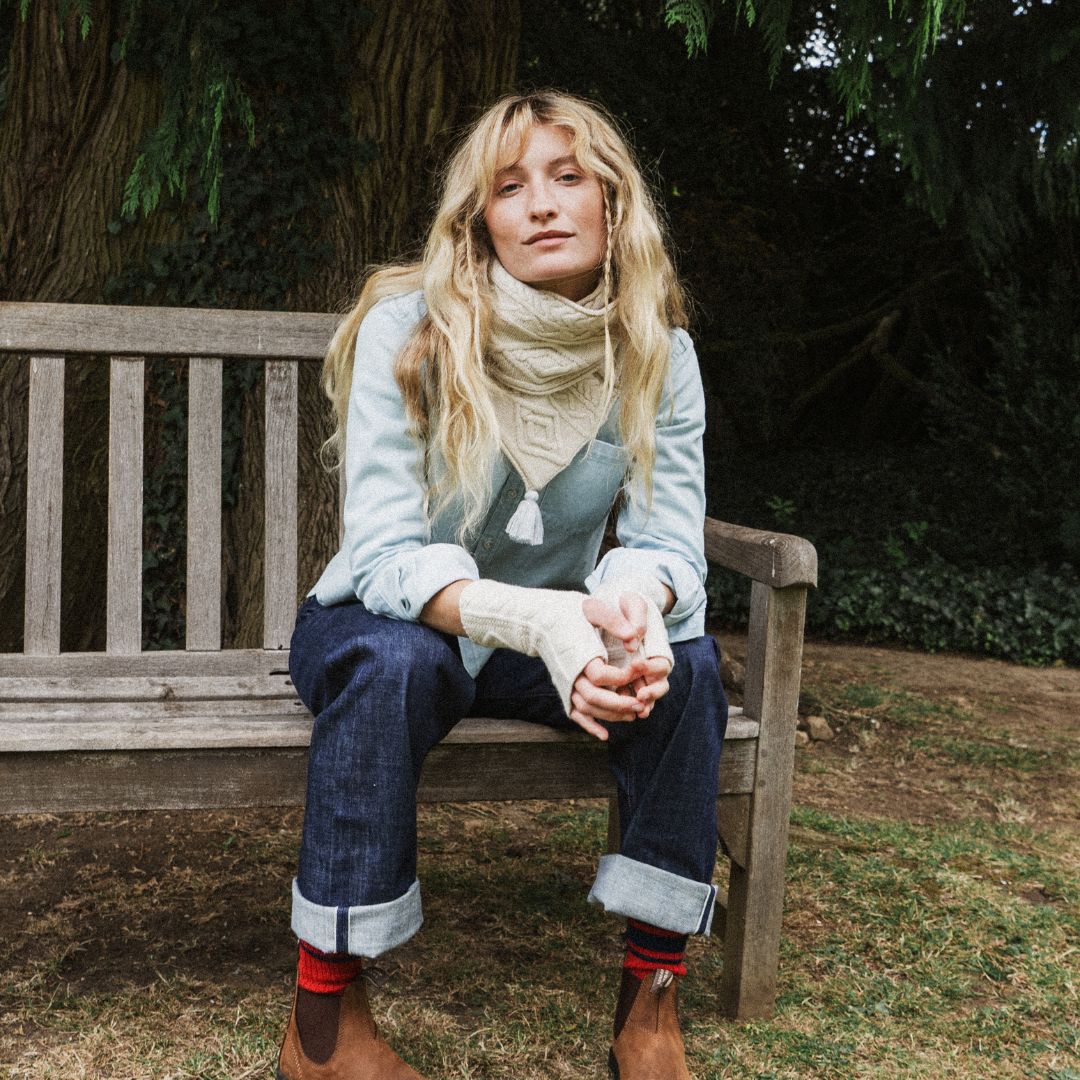 woman sitting on a bench wearing a cream scarf and blue jeans.