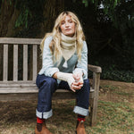 woman sitting on a bench wearing a cream scarf and blue jeans.