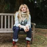 woman sitting on a bench wearing a cream scarf and blue jeans.