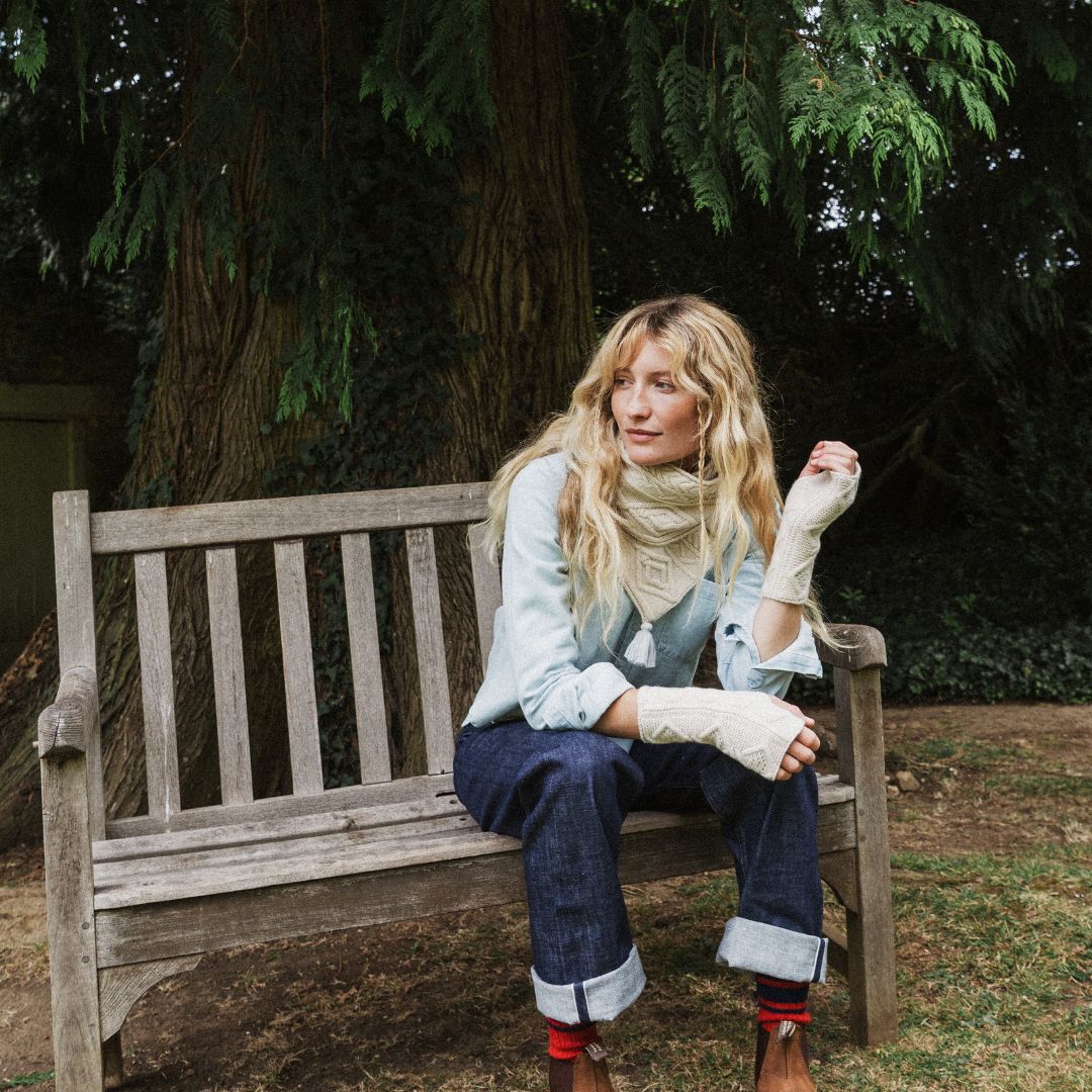 woman on a bench wearing and cream cable knit scarf.