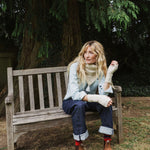 woman on a bench wearing and cream cable knit scarf.