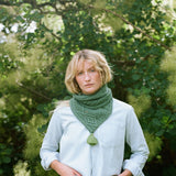 A lady with blonde hair standing in front of a tree wearing a green scrarf.