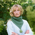 A smiling lady standing with rms folded wearing a green cable knit scarf.