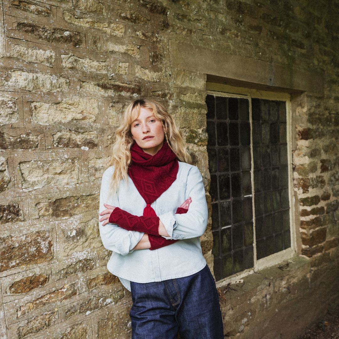 woman standing by a wall wearing a red cable knit scarf and blue jeans.