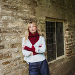 woman standing by a wall wearing a red cable knit scarf and blue jeans.
