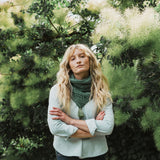 a woman standing beside a bush wearing a green cable knit scarf.