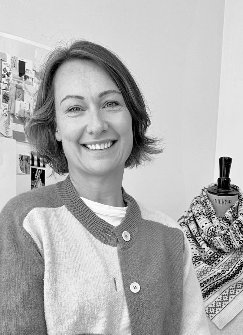 black and white photogrpah of a smiling lady standinging in a knit studio waering a check cardigan.