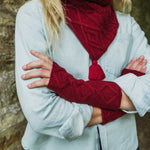 A person wearing a light blue button-up shirt, a deep red cable-knit scarf with a tassel, and matching deep red cable-knit fingerless wrist warmers, with arms crossed.