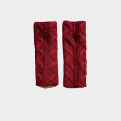 A pair of deep red cable-knit wrist warmers with a central split opening, displayed flat against a light gray background.