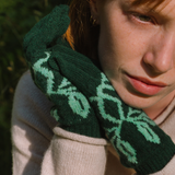 Person wearing green patterned gloves with a blurred natural background