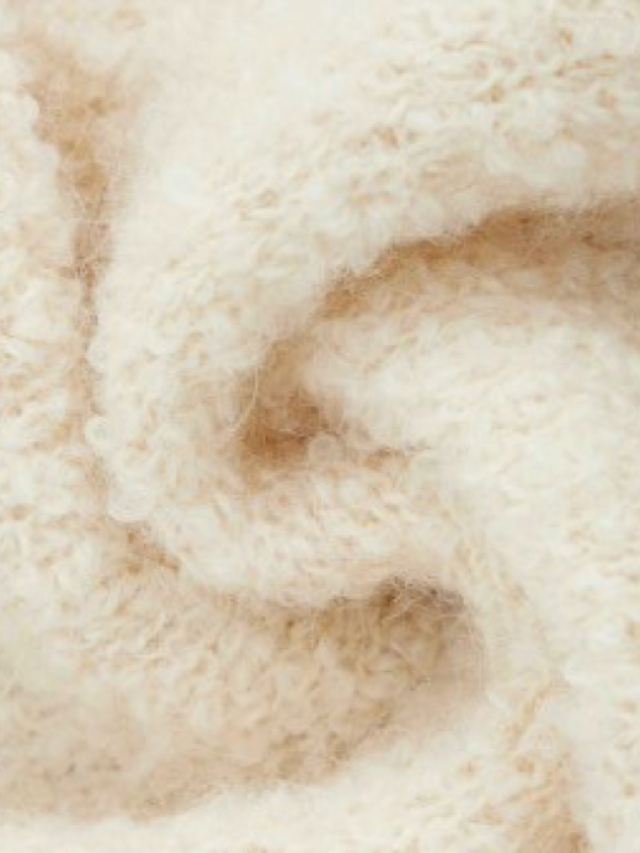 A close-up of soft, fluffy knit fabric in a warm cream or off-white color, showing the texture and folds of the material.