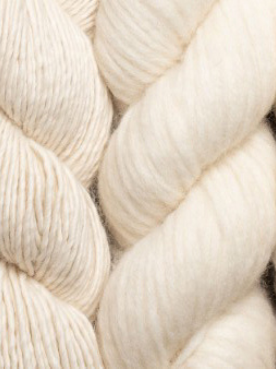 A close-up of thick, soft yarn in a warm off-white or cream color, showing the texture of the fibers.