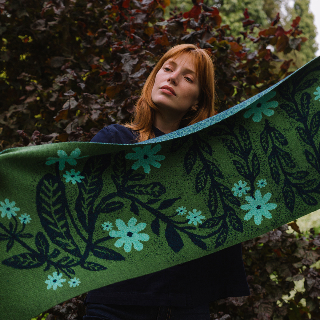 Woman holding a green scarf with floral patterns against a natural background