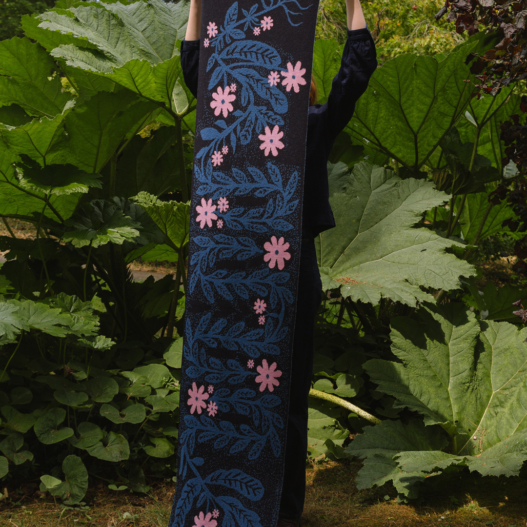 Person holding a scarf with pink floral patterns against a green leafy background
