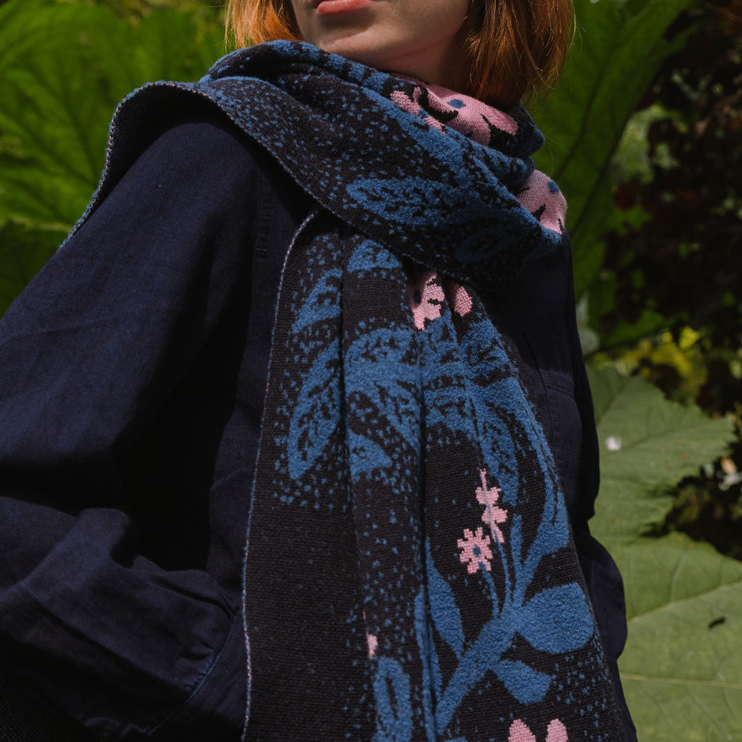 Person wearing a dark blue floral-patterned scarf with pink flowers against a green leafy background