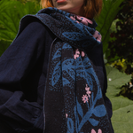 Person wearing a dark blue floral-patterned scarf with pink flowers against a green leafy background