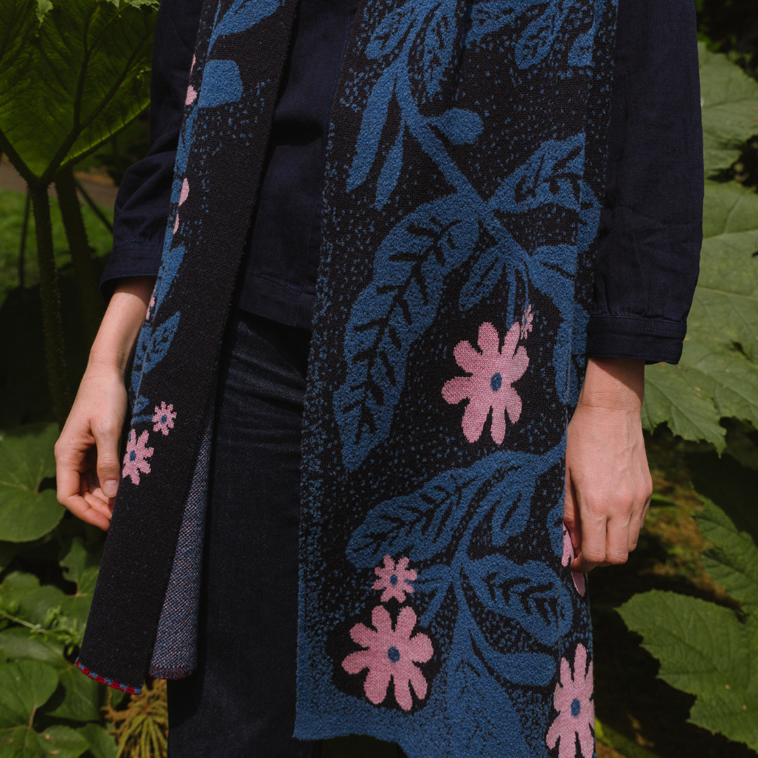 Person wearing a dark scarf with floral patterns in blue and pink against a green leafy background