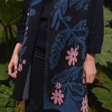 Person wearing a dark scarf with floral patterns in blue and pink against a green leafy background